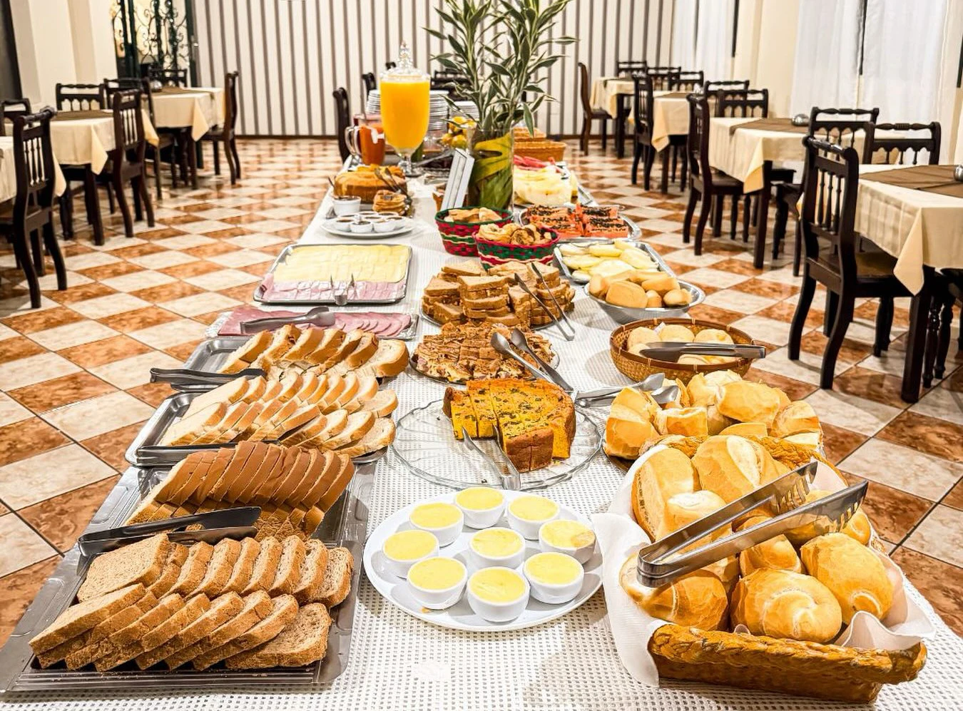 Salão de café da manhã do Presidente Hotel com buffet de pães, frutas, frios e bolos